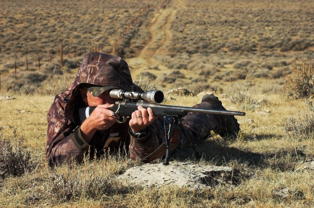 a hunter laying in a field using the best elk hunting rifle